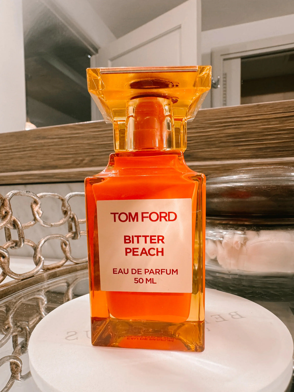 BRight orange perfume bottle by Tom Ford Bitter Peach on a mirrored tray.