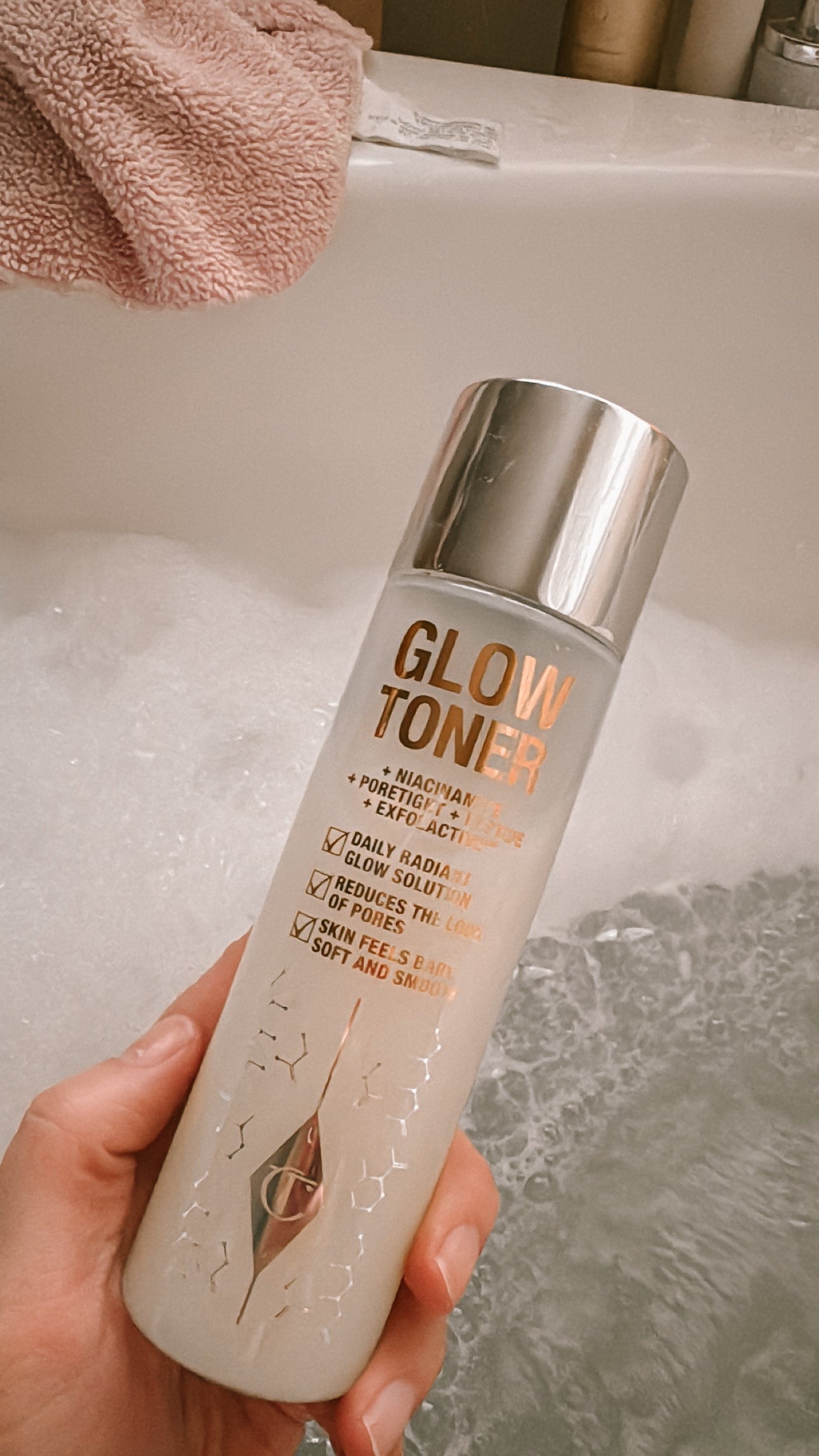Glow Toner by Charlotte Tilbury in a woman's hand over a bubble bath.