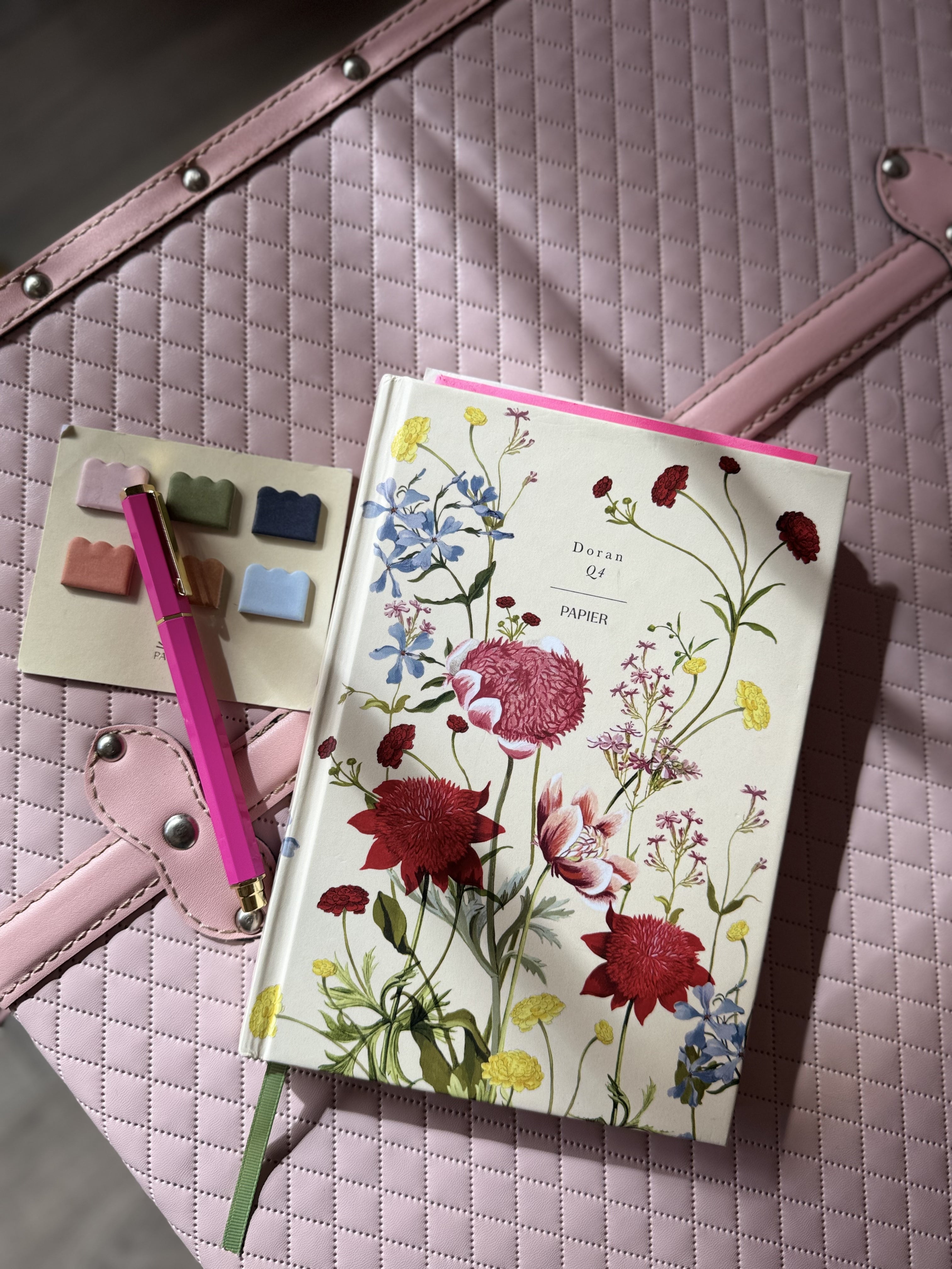 flower covered journal with a pen and sticky tabs on a pink quilted suitcase