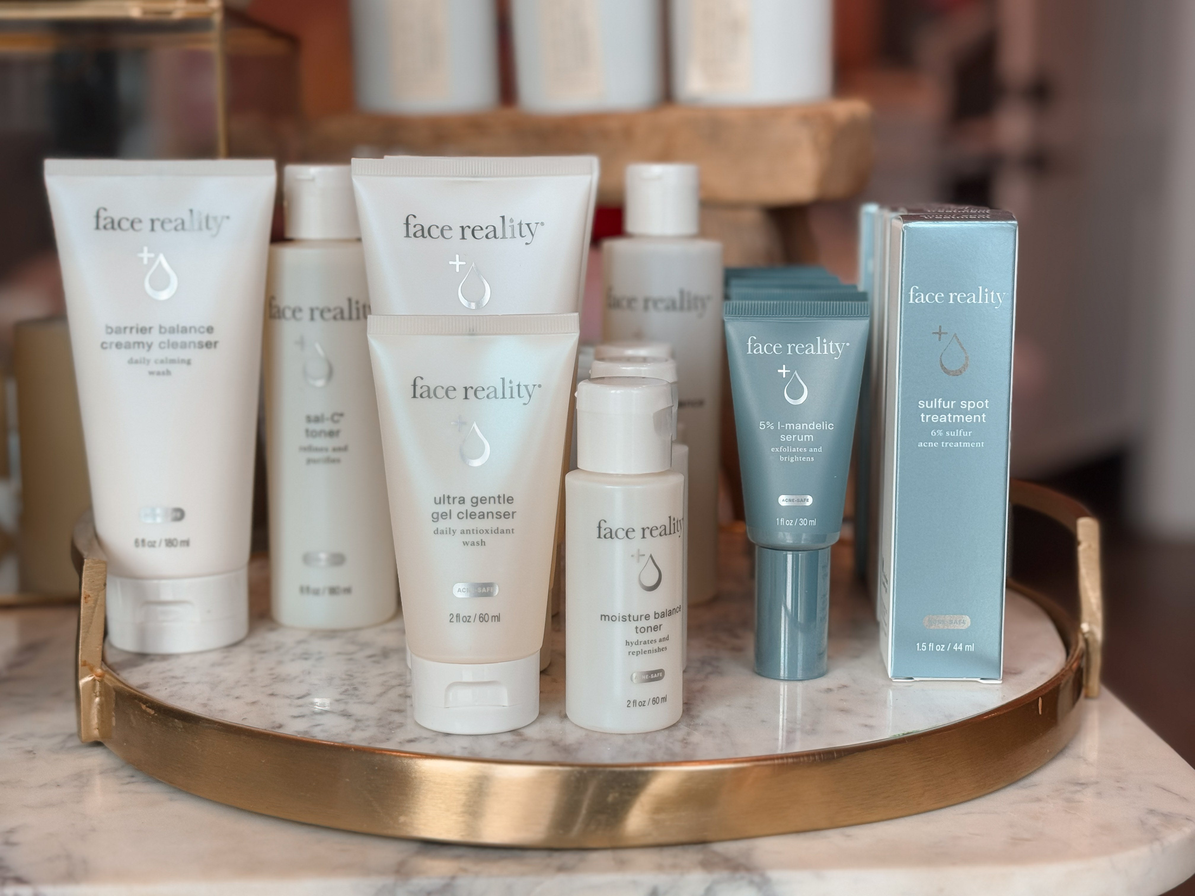 Collection of 'face reality' skincare products on a marble tray. Products from left to right Barrier balance creamy cleanser, SAL-C toner, Ultra gentle gel cleanser, moisure balance toner, 5% l-mandelic serum, face reality sulfur spot treatmetn 6% sulfur acne treatment.