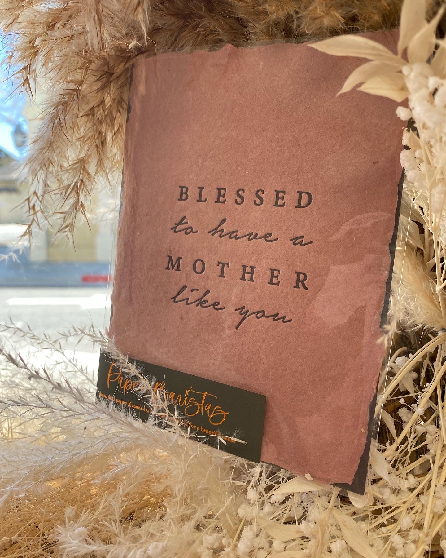 Pink card with 'Blessed to have a mother like you' text, surrounded by dried plants.