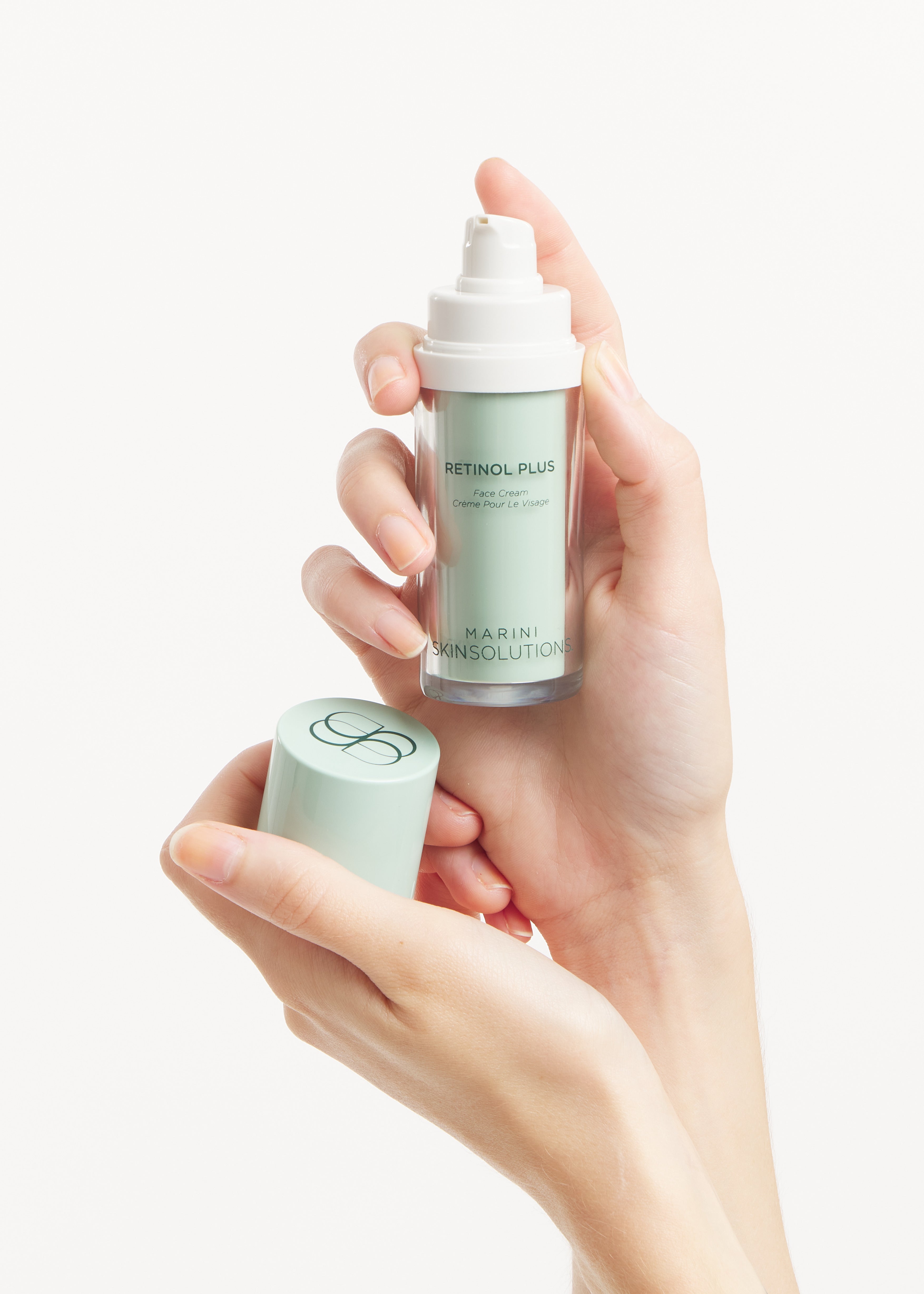 Hand holding Retinol Plus bottle and cap with a plain background