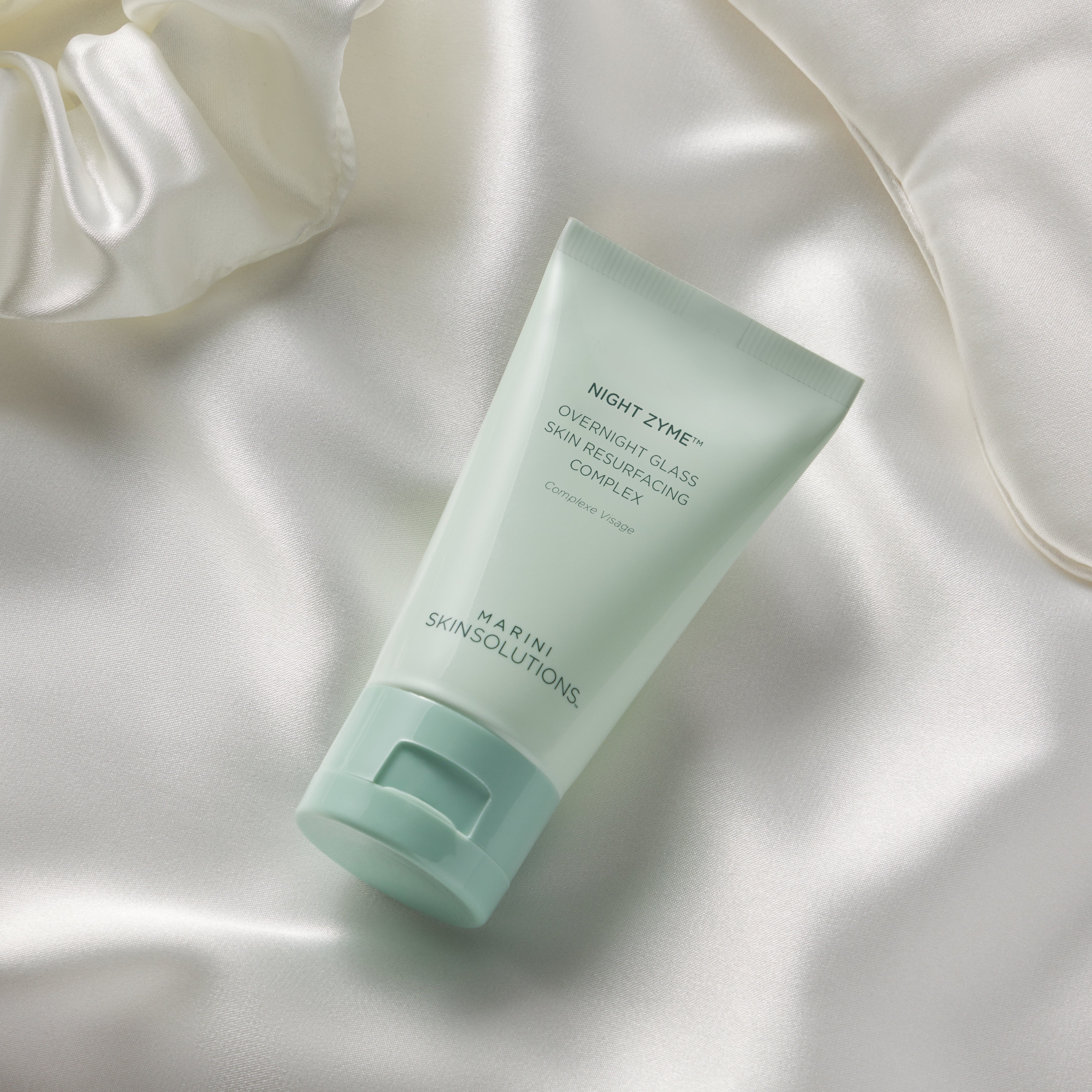 Green skincare tube on a soft white fabric background