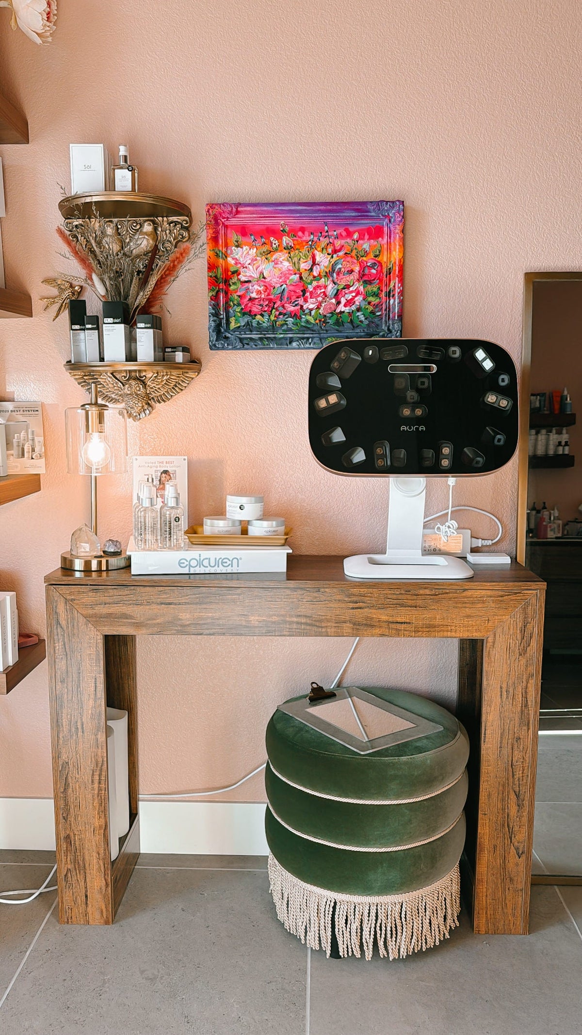 Aura Reality 3D skin scanner on a stand next to a wood console table with Epicuren and Söl skincare products, in a pink-walled treatment room at Doran Poma Aesthetics in Marina, California.