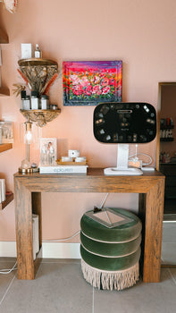 Aura Reality 3D skin scanner on a stand next to a wood console table with Epicuren and Söl skincare products, in a pink-walled treatment room at Doran Poma Aesthetics in Marina, California.