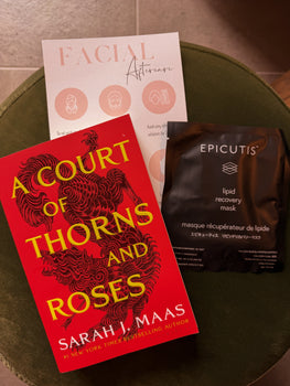 Flat lay of A Court of Thorns and Roses by Sarah J. Maas next to an Epicutis Lipid Recovery Mask sachet and a Facial Aftercare card, styled on a green velvet ottoman.