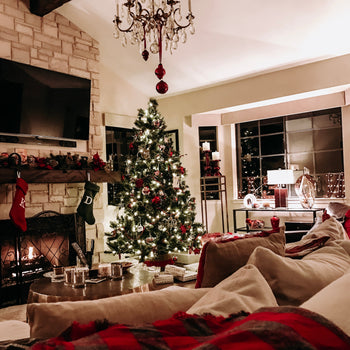 Holiday decorations in a living room.  Fire burning with a tree and red decorations spread about.  Couch is covered in red tartan pillows and blanket.