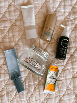 a bundle of empty skincare products on a pink blanket.  products include Plated skin, Hydropeptide Nimni Day, L'occitain body and hands creams, Omorovicza face wash and Hydrafacial Keravive leave on spray