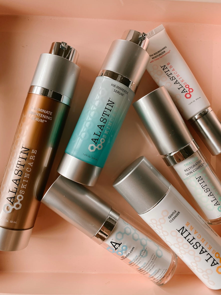 a collection of empty Alastin Skincare products spilled on a pink tray.