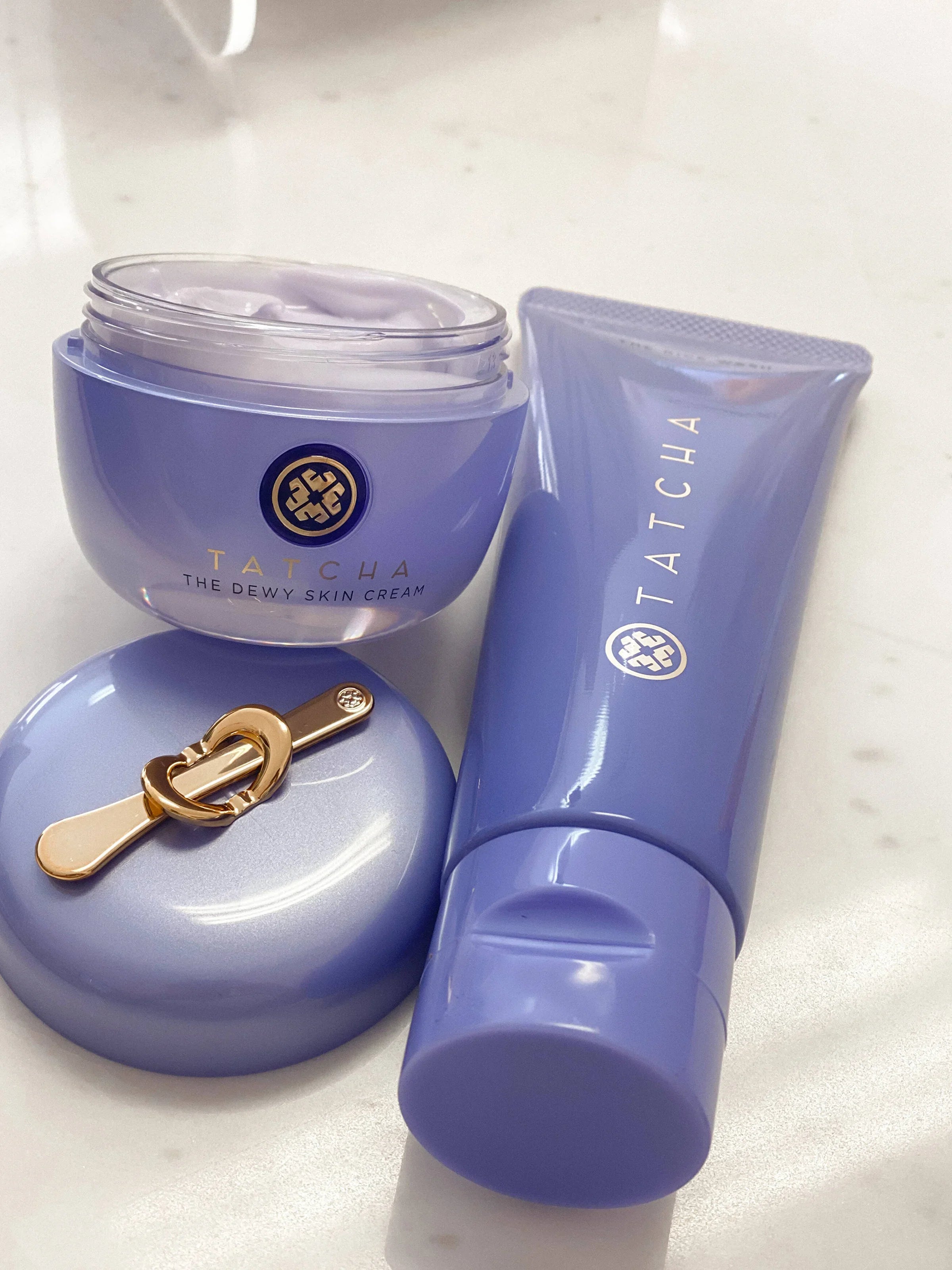 Tatcha purple bottles of the dewy skin cream and rice wash cleanser on a marble table