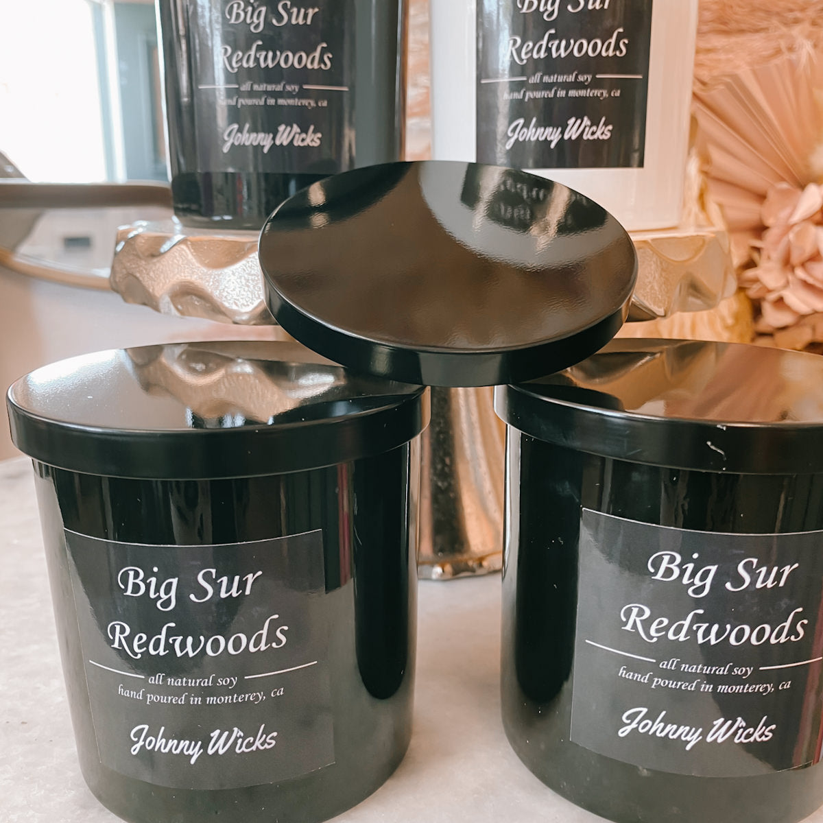 Black containers labeled 'Big Sur Redwoods' by Johnny Wicks on a reflective surface.