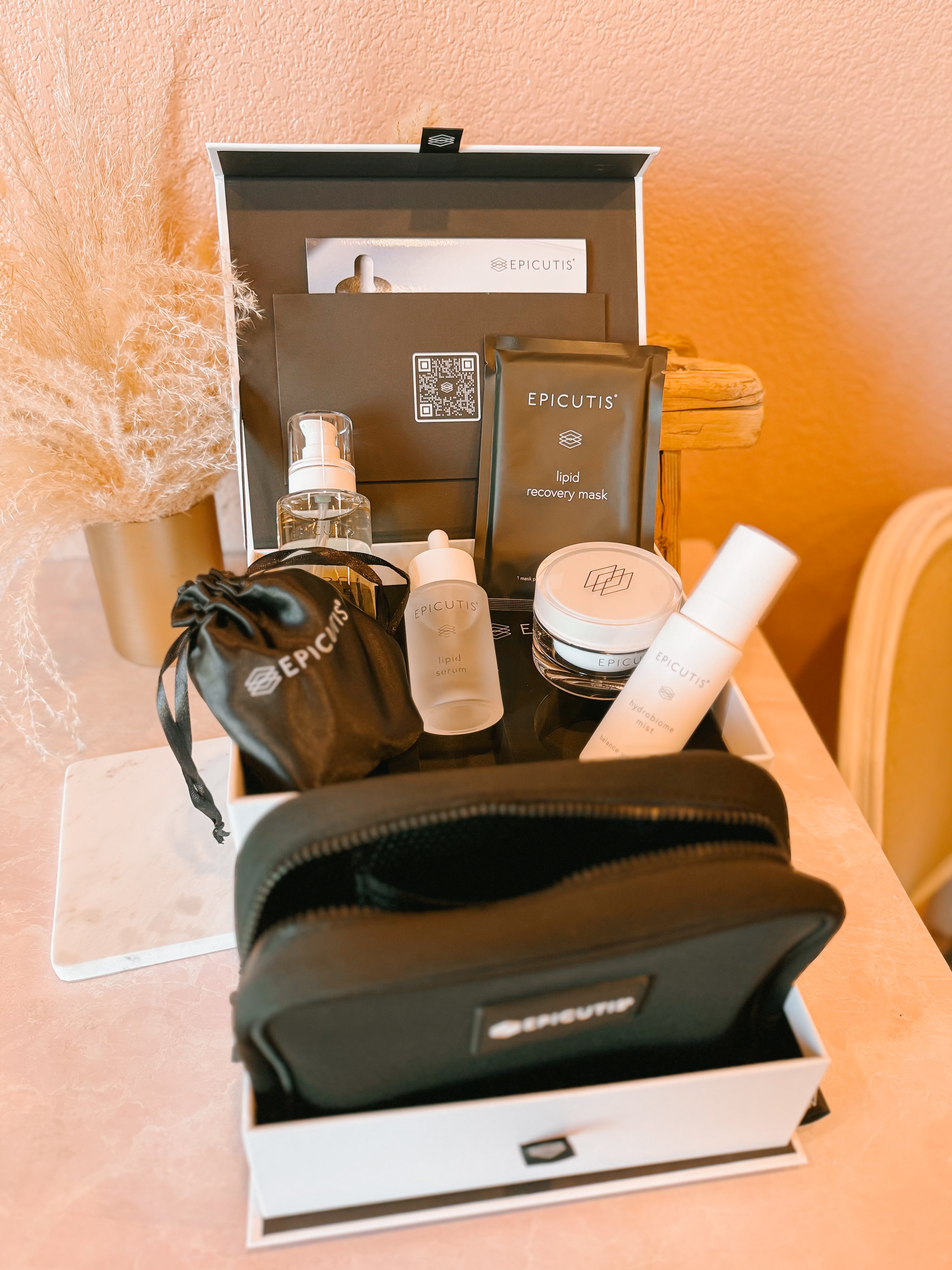 Set of Epicuts skincare products in a box on a pink surface.  Products include the cleansing oil, lipid serum, Hyvia Face Cream, Hydrobiome mist and lipid recovery mask. 