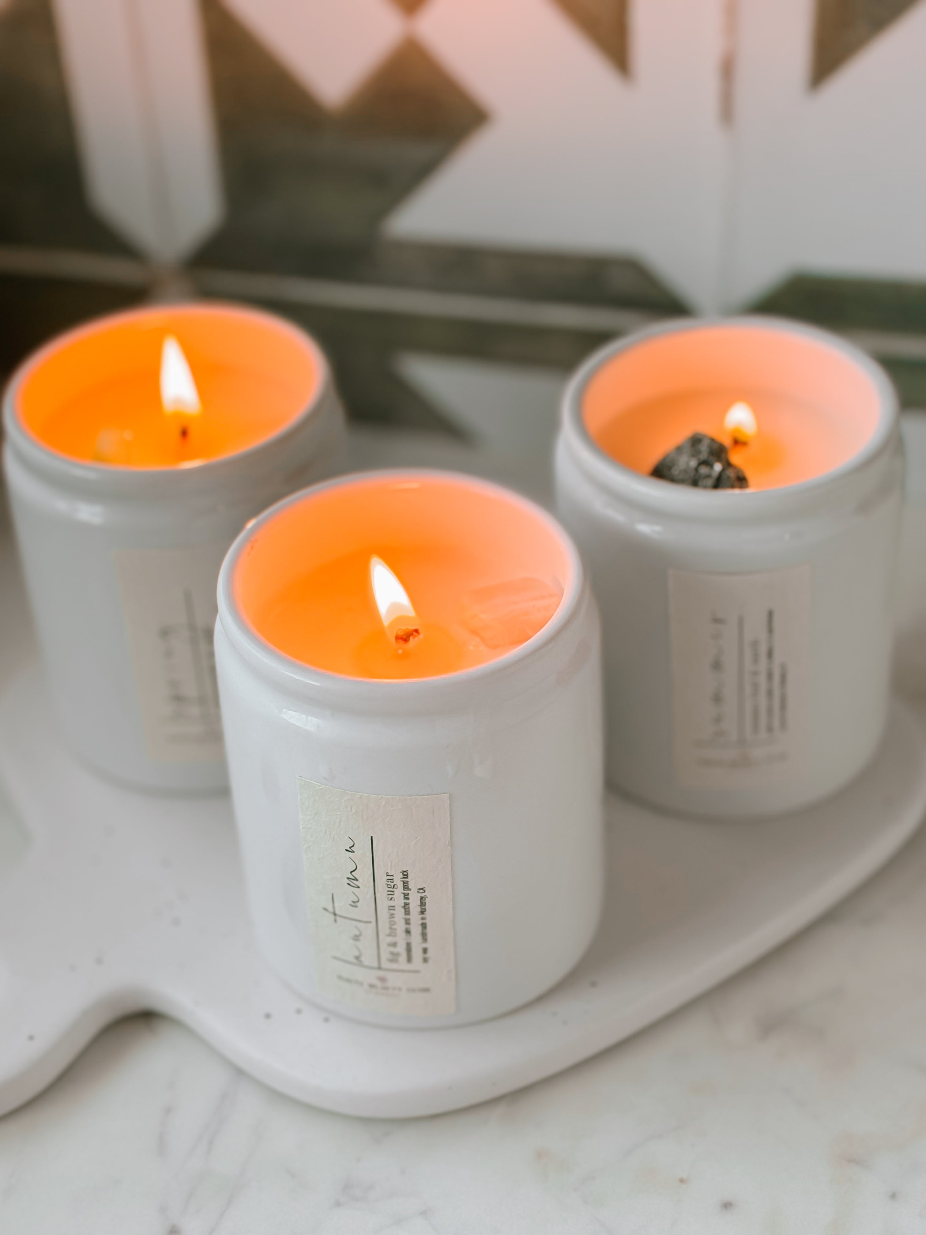 Three lit candles in white containers on a marble surface with a blurred background