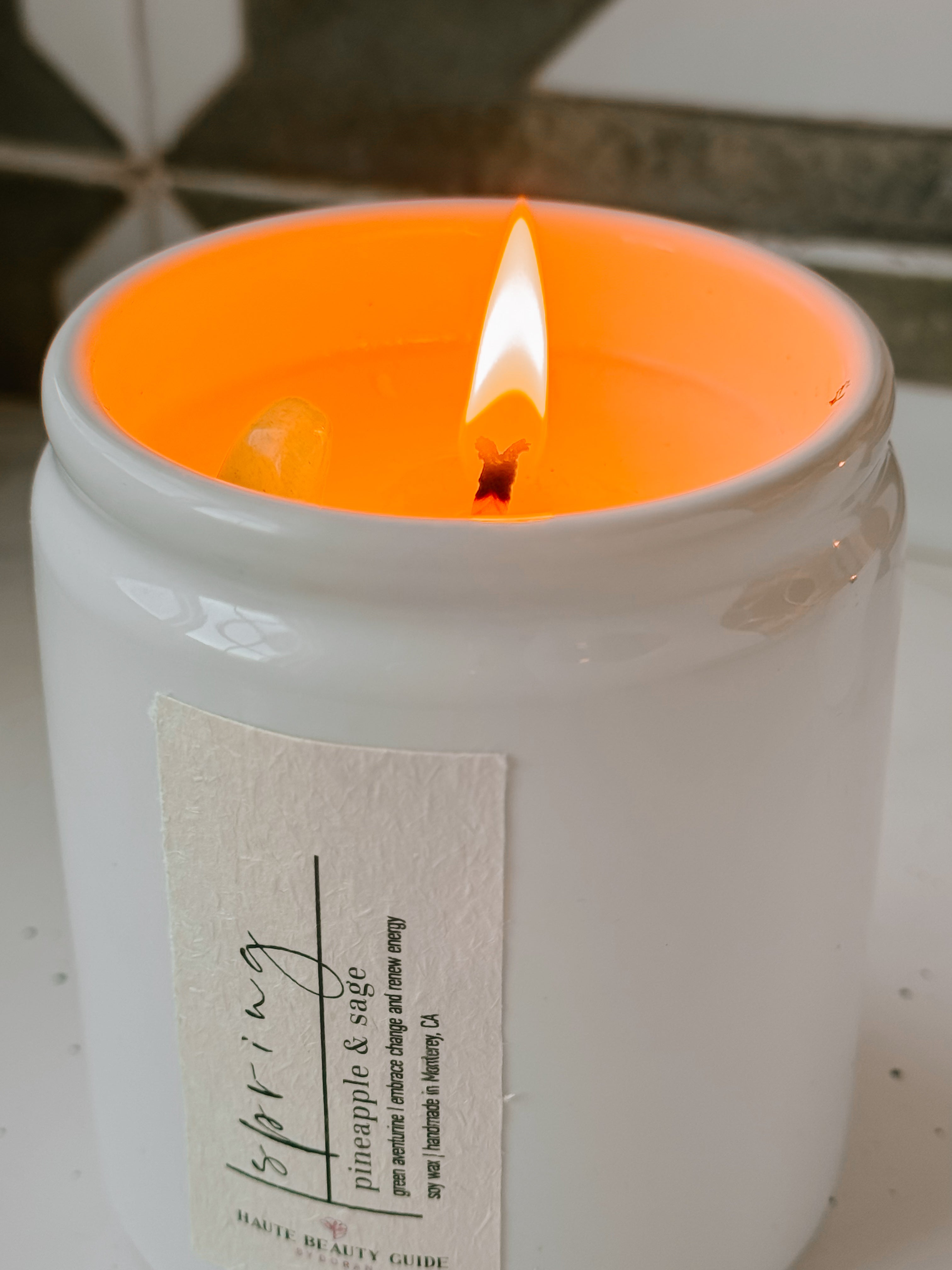 A Spring Candle in a white jar with an orange interior, lit, on a neutral background
