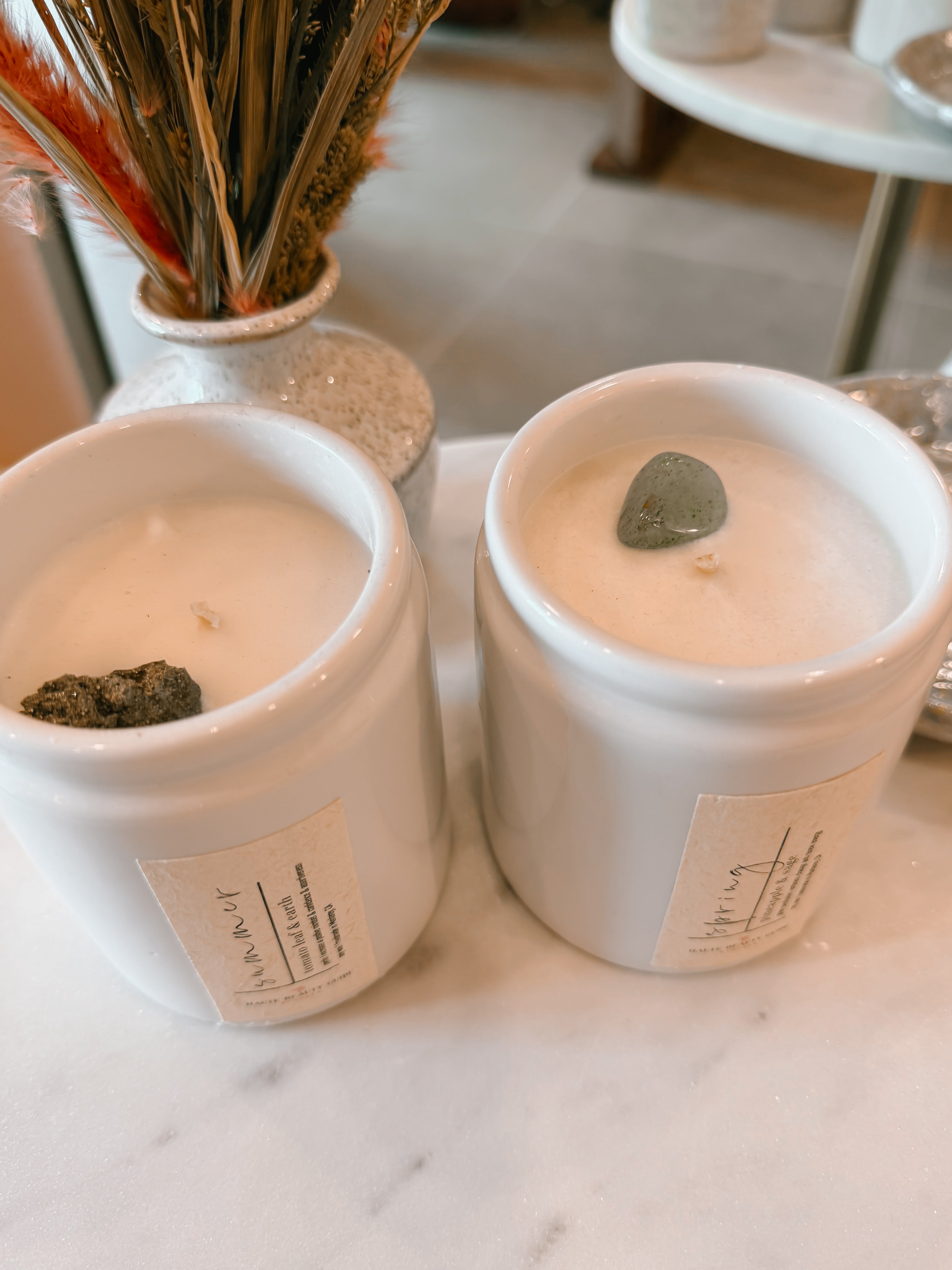Two white candles with decorative stones on top, placed on a marble surface.
