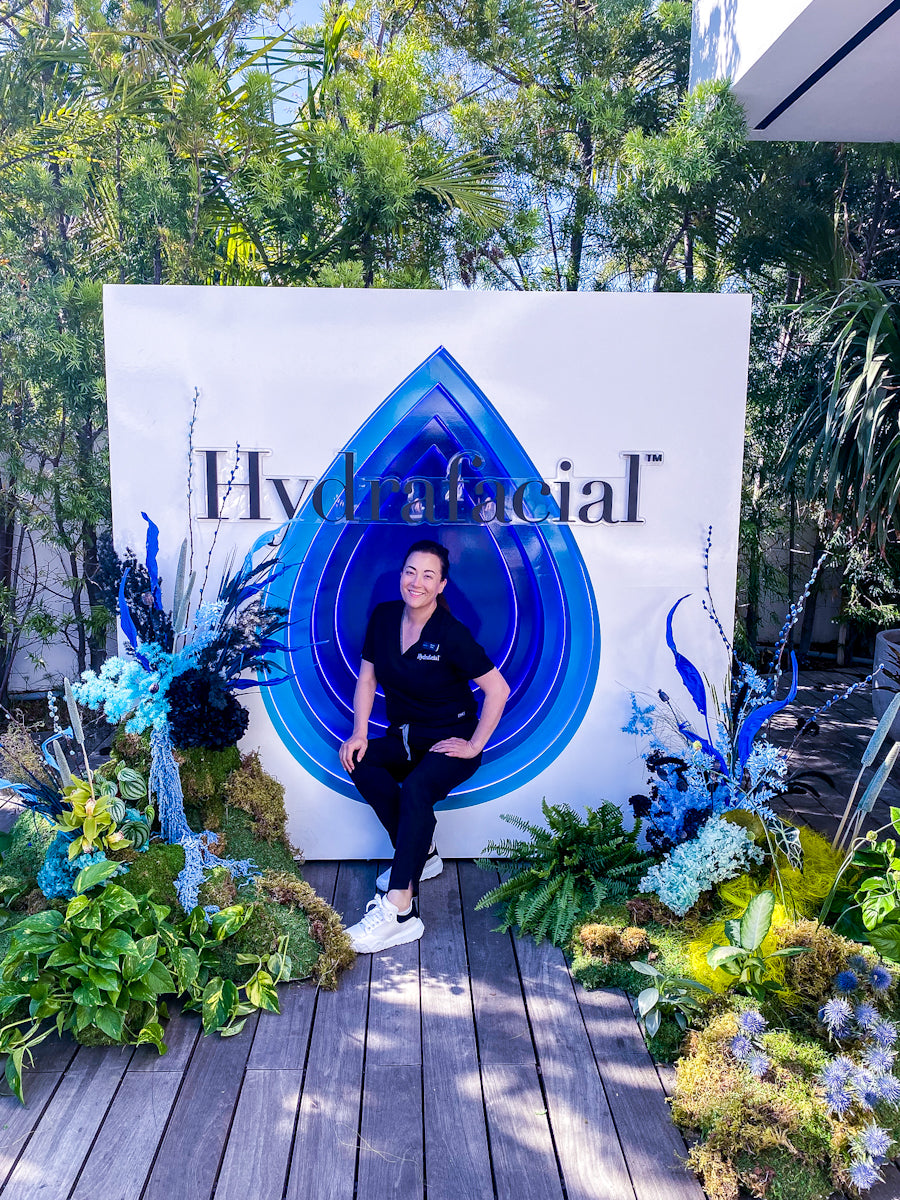Person posing in front of a 'Hydrafacial' branded backdrop with decorative elements.